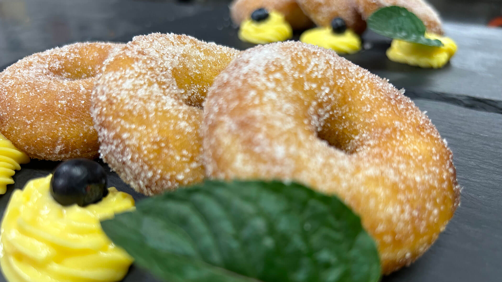Sugary donuts on a slate plate with yellow cream, blueberries, and green leaves as garnish. - Il Leone Restaurant