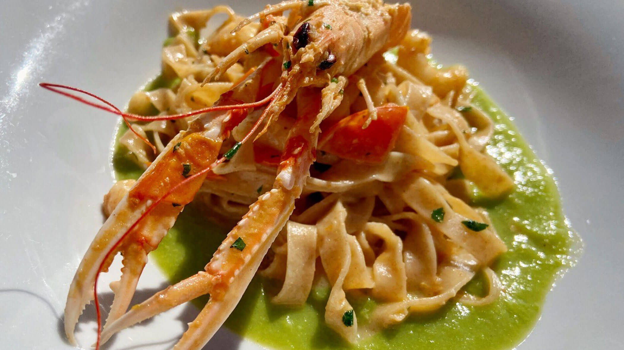 Tagliatelle pasta with a whole langoustine, cherry tomatoes, and green sauce on a white plate. - Il Leone Restaurant