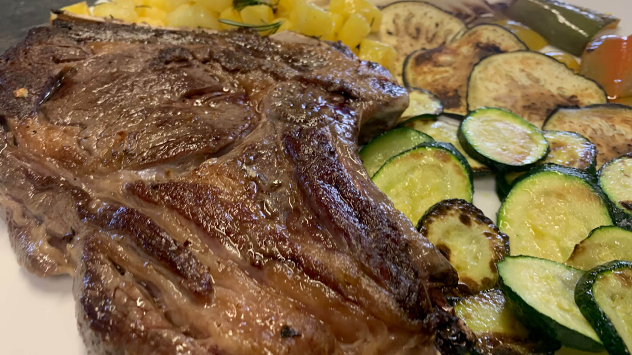 Grilled steak served with sautéed zucchini, yellow squash, and roasted eggplant slices on a plate. - Il Leone Restaurant