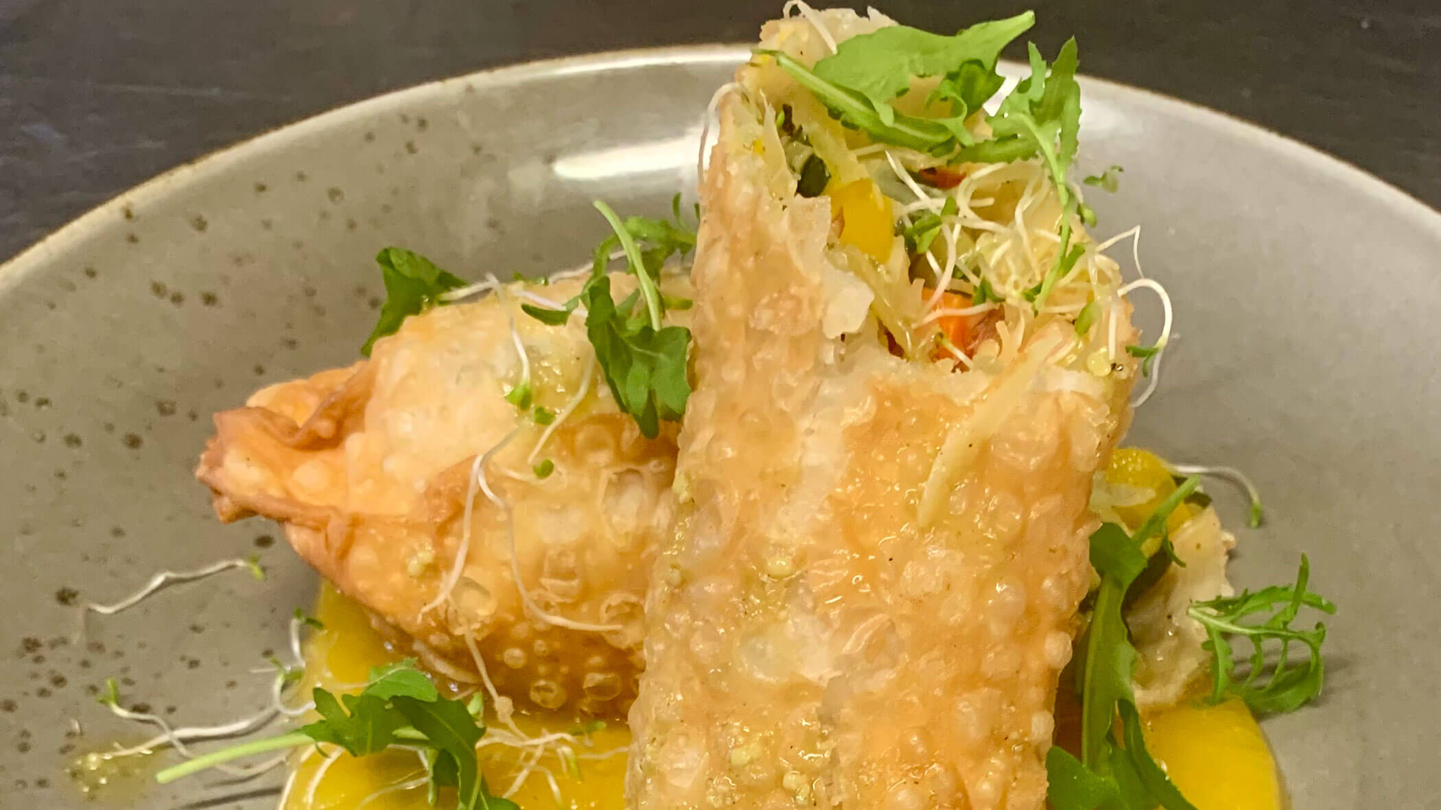 Crispy spring roll cut open, filled with vegetables, served on a grey plate with fresh greens and sprouts. - Il Leone Restaurant
