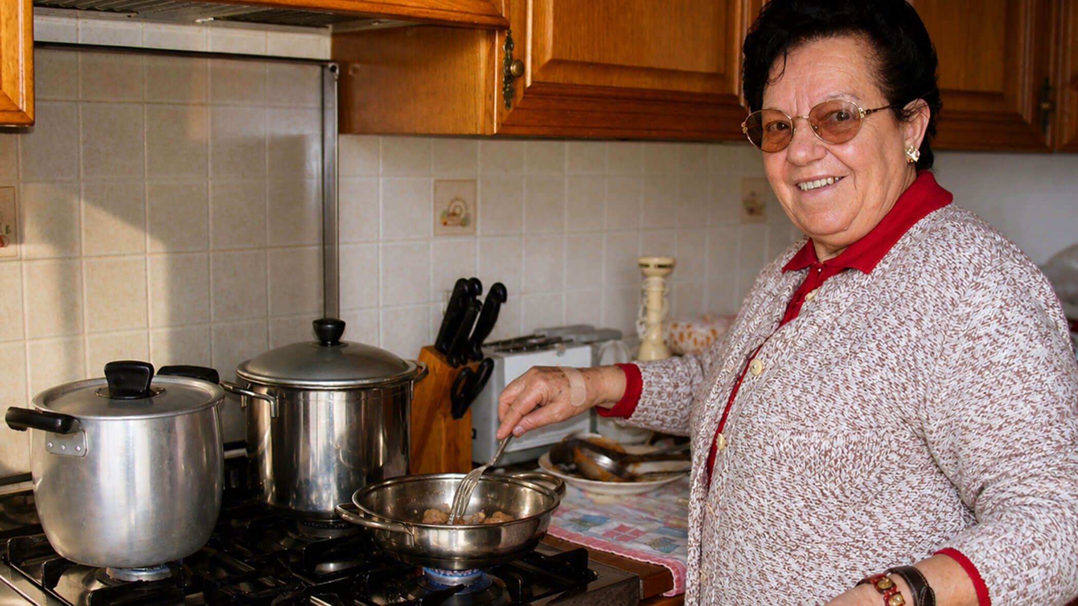 Smiling woman cooking at a stove with pots and a pan in a home kitchen. - Il Leone Restaurant