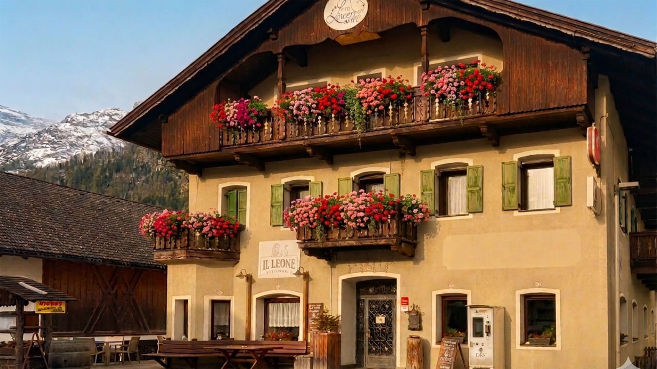 Charming alpine building with flower-filled balconies and green shutters, set against a mountain backdrop. - Il Leone Restaurant