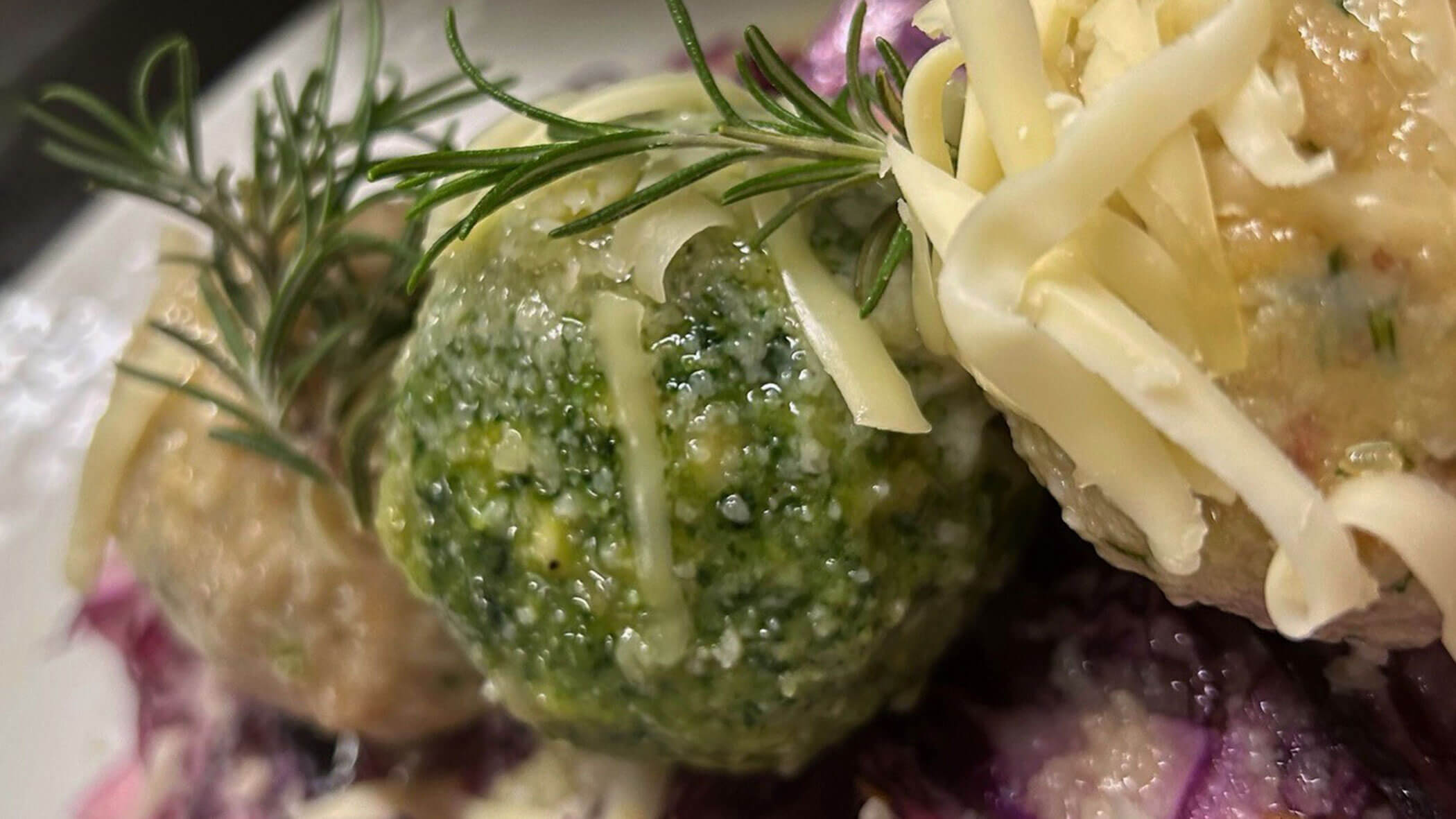 Three dumplings garnished with rosemary and shredded cheese, served on a bed of red cabbage. - Il Leone Restaurant