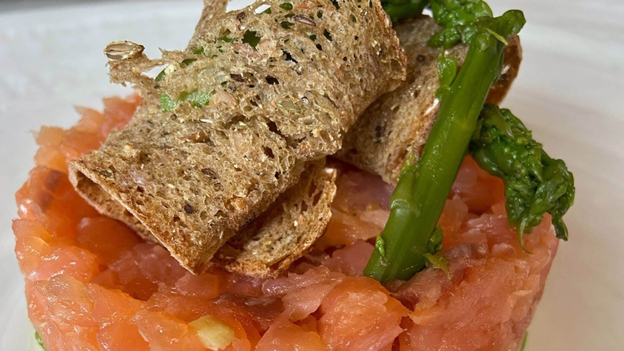 Salmon tartare topped with whole grain crackers and asparagus on a white plate. - Il Leone Restaurant
