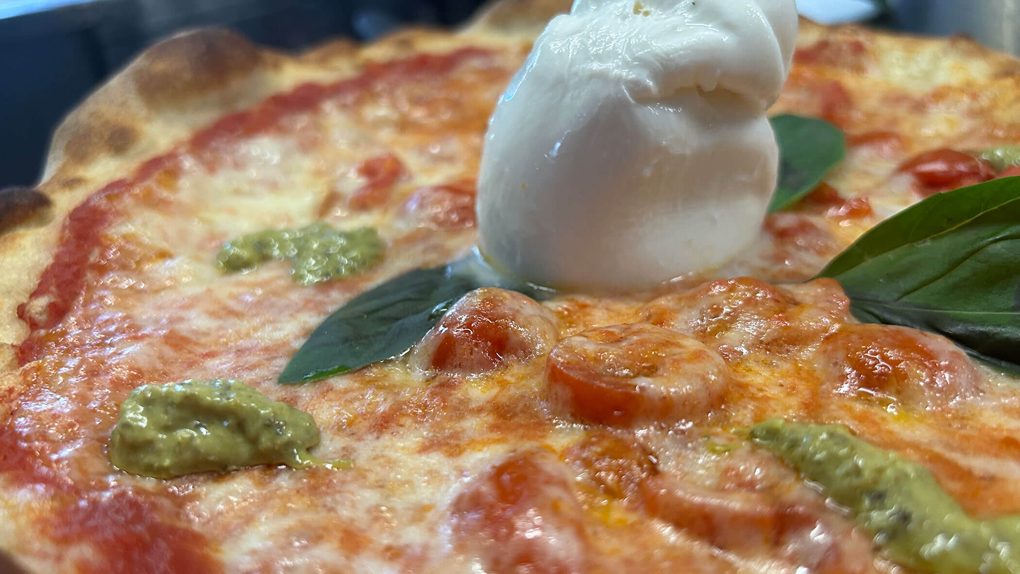 Close-up of a pizza topped with cherry tomatoes, basil leaves, pesto, and a ball of fresh mozzarella cheese. - Il Leone Restaurant