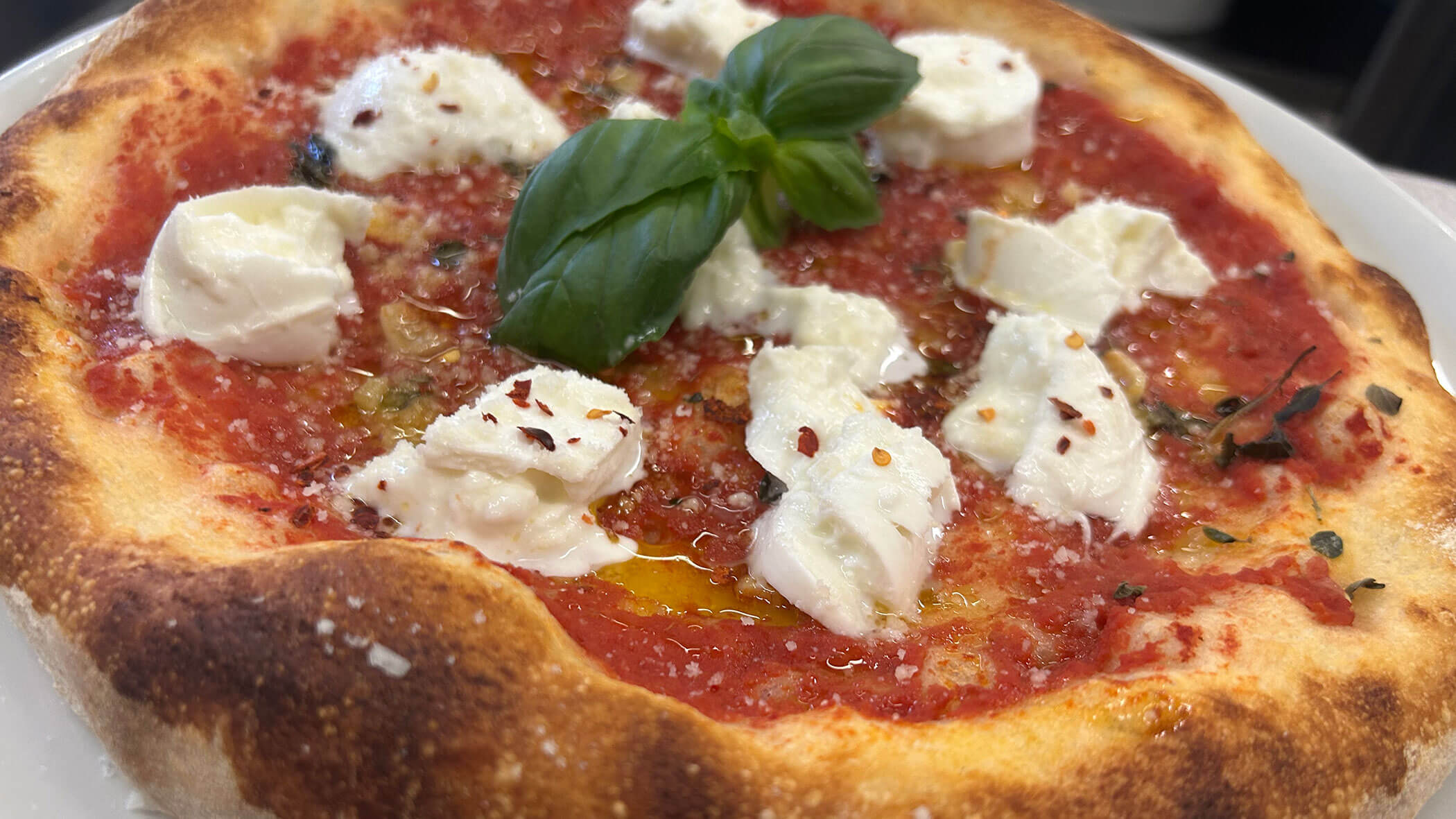 Nahaufnahme einer Pizza Margherita mit Tomatensauce, Mozzarella, Basilikumblättern und einer goldbraunen Kruste. - Il Leone Restaurant