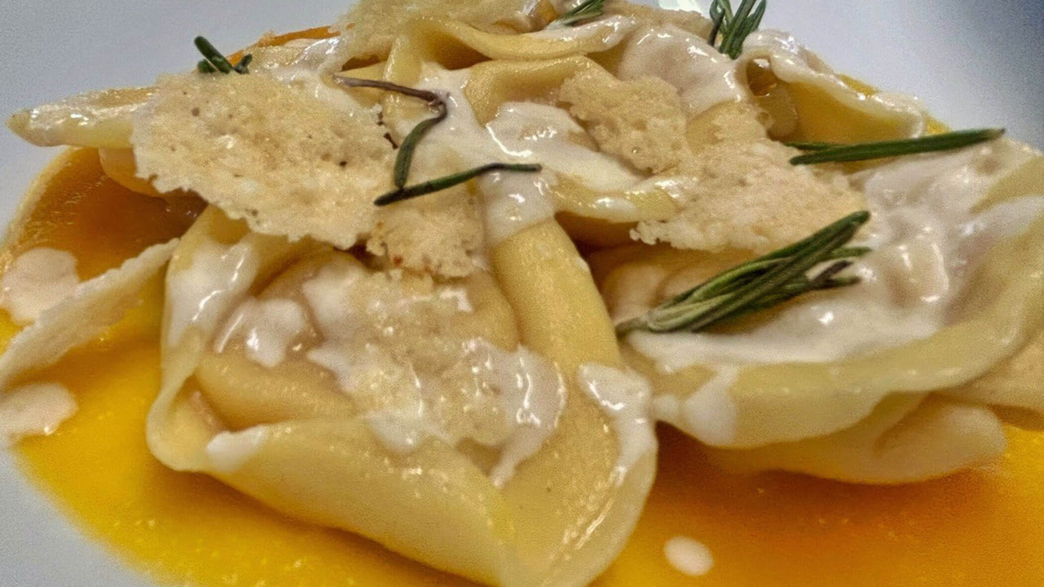 Close-up of tortellini with cream sauce, crispy cheese, and rosemary on an orange-colored purée. - Il Leone Restaurant