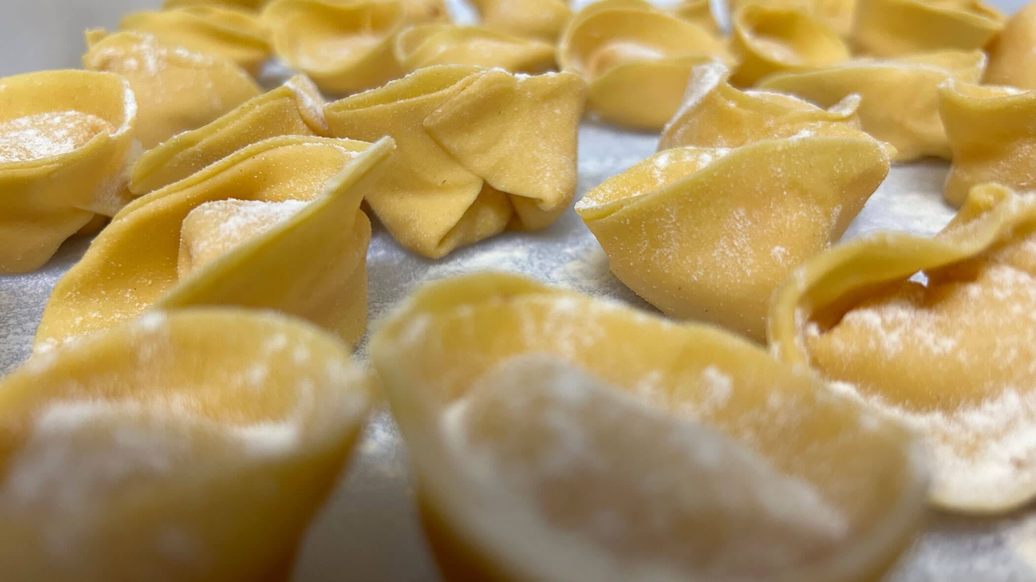 Close-up of fresh, uncooked tortellini pasta pieces on a floured surface, ready for cooking. - Il Leone Restaurant