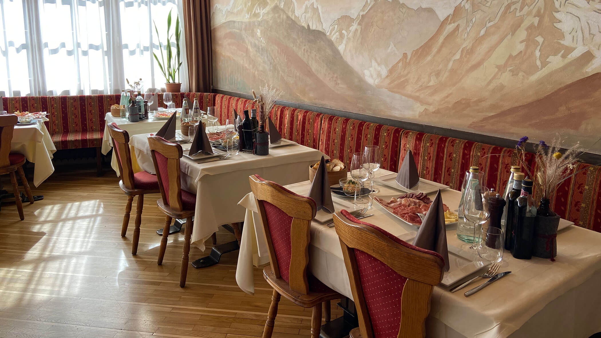 Elegant restaurant with red chairs, set tables, and a mountain mural on the wall. Sunlight streams in. - Il Leone Restaurant