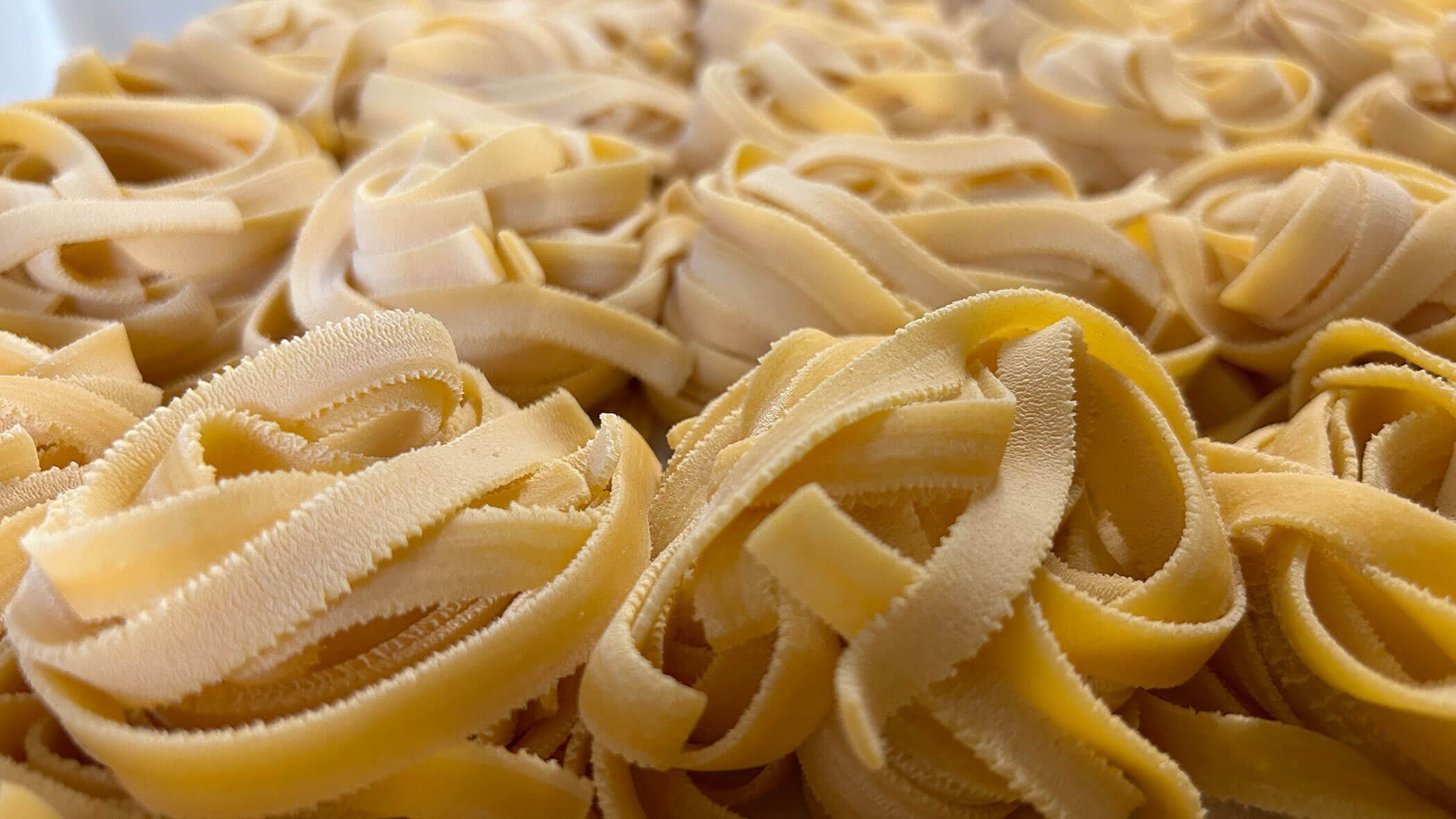 Close-up of uncooked tagliatelle pasta nests arranged closely together. - Il Leone Restaurant